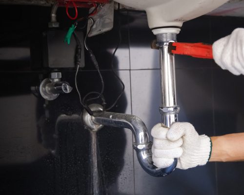 Plumber fixing white sink pipe with adjustable wrench.